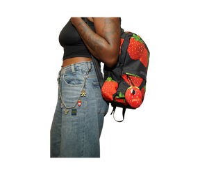A person wearing a black crop top and light-wash denim jeans with a chain belt and a strawberry-patterned backpack, shown from the waist up against a plain white background.