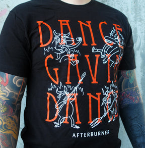 close up of man with tattoos on both arms standing in front of a cement wall wearing a black tee with a full chest print that says dance gavin dance in stacked orange print and has four white outlined characters dispersed around and says afterburner on the bottom